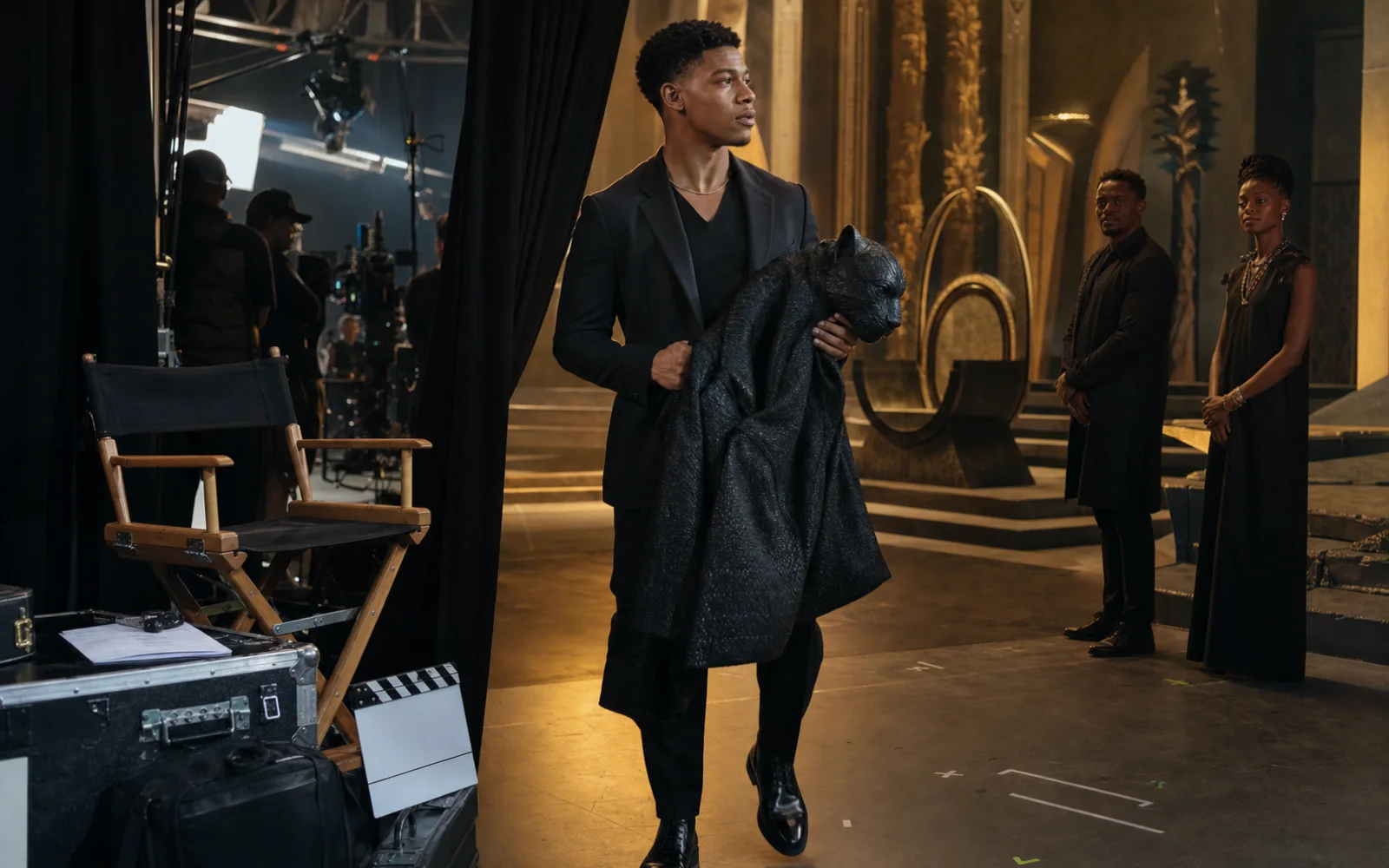 Jeune acteur noir entrant sur un plateau de cinéma avec un manteau de scène félin, entre coulisses sombres et décor éclairé