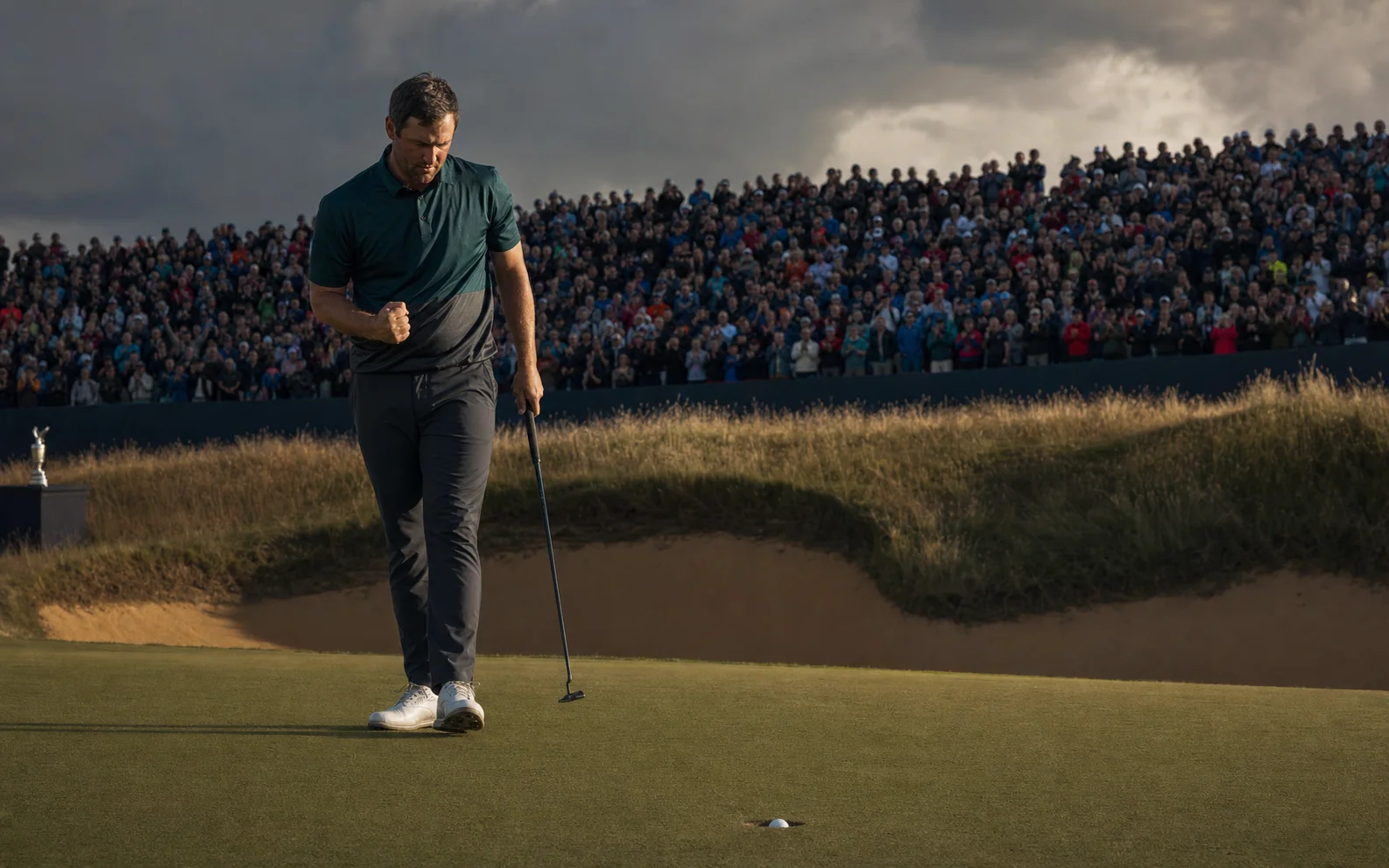 Un golfeur serre le poing après le putt décisif sur un green de links devant une foule compacte