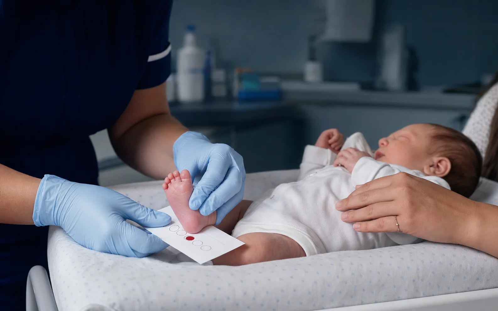 Une infirmière recueille une goutte de sang au talon d’un nouveau-né soutenu par la main de son parent